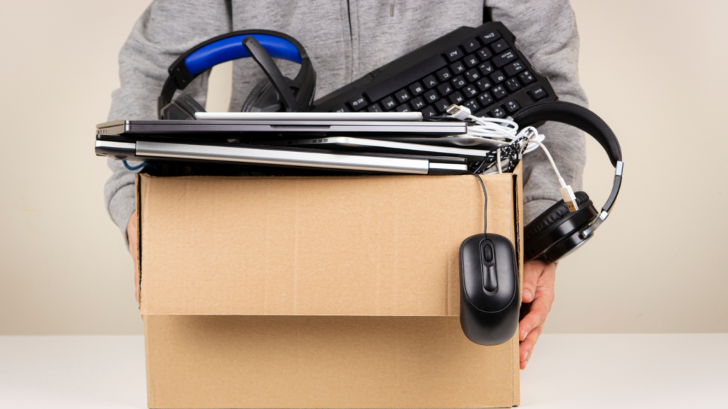 Een man die zijn gedoneerde laptops, toetsenbord, koptelefoon en ander materiaal aflevert in een doos